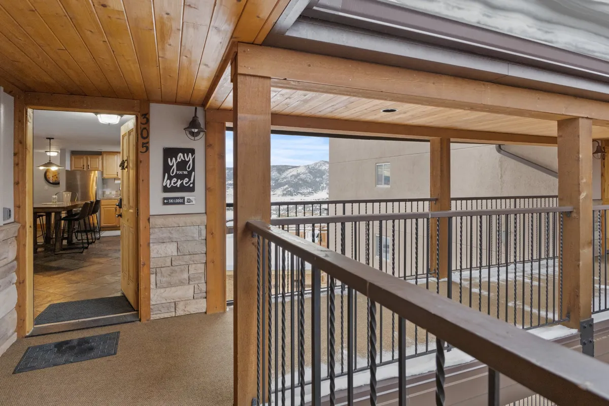 This image shows the entrance door of the property with a decorative sign, set against a backdrop of scenic mountain views. The perspective is inviting, suggesting a seamless transition between the property and the natural landscape beyond.