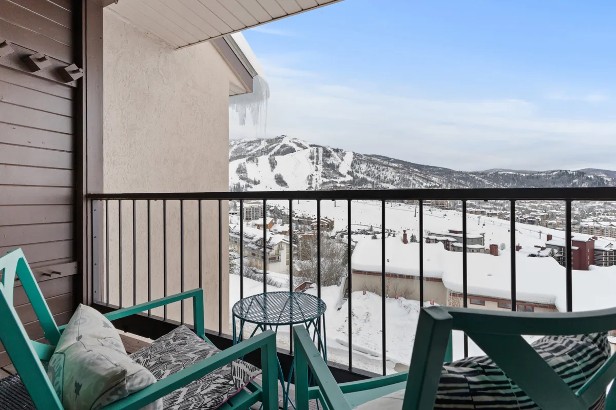 A serene balcony scene looking out over snow-covered mountains and the town below. The balcony itself is inviting, with seating for relaxing and soaking in the alpine panorama—ideal for après-ski or morning coffee with a view.