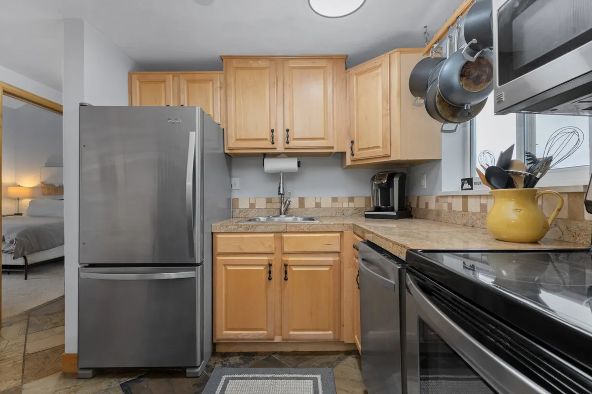 A close-up view of a sleek kitchen featuring a stainless steel refrigerator, granite countertops, and well-organized cabinets. Culinary gadgets and kitchen utensils are neatly arranged, emphasizing readiness for group cooking and entertaining.