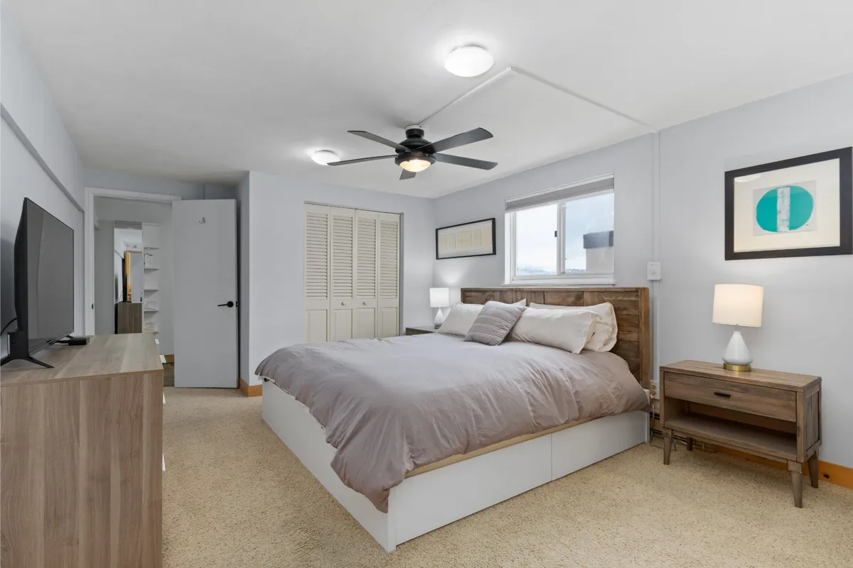 A tranquil bedroom featuring a plush bed with soft linens, a nightstand, a wall-mounted television, and a window letting in abundant natural light. Calming artwork and thoughtful touches create an inviting environment for relaxation and restful sleep.