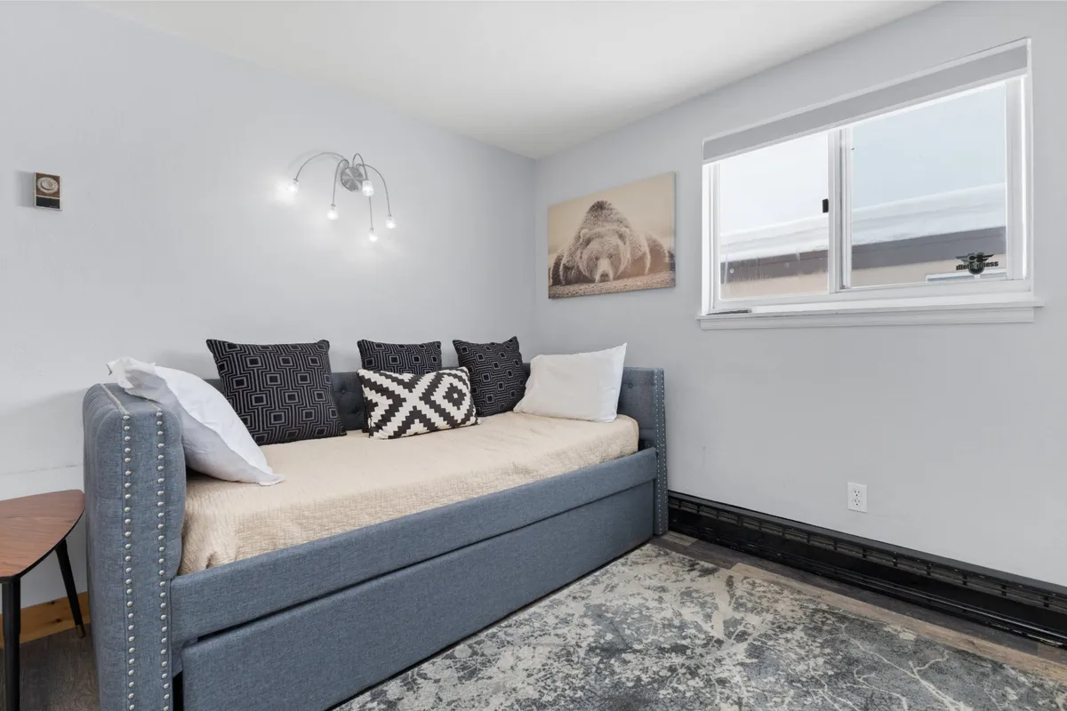 An inviting loft area featuring a stylish daybed with decorative pillows, vibrant wall art, and a window that fills the space with natural light. The layout is flexible—ideal for lounging, reading, or transforming into an extra sleeping area.