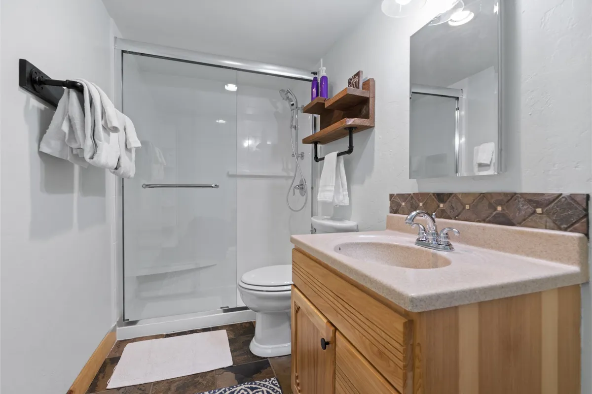 A bright, modern laundry room with a shower area, sink, wooden cabinet, and open shelves. Family members can be seen preparing for a refreshing shower or sorting laundry, reflecting practical features that support extended, comfortable stays.