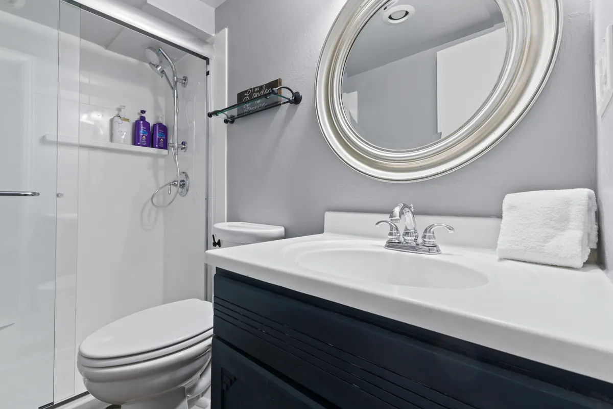 A modern bathroom with a large round mirror, a sleek sink, glass shower enclosure, and dark cabinetry. The clean design and inviting ambiance suggest a refreshing and comfortable space for guests to unwind and refresh, whether after a day on the slopes or a summer hike.