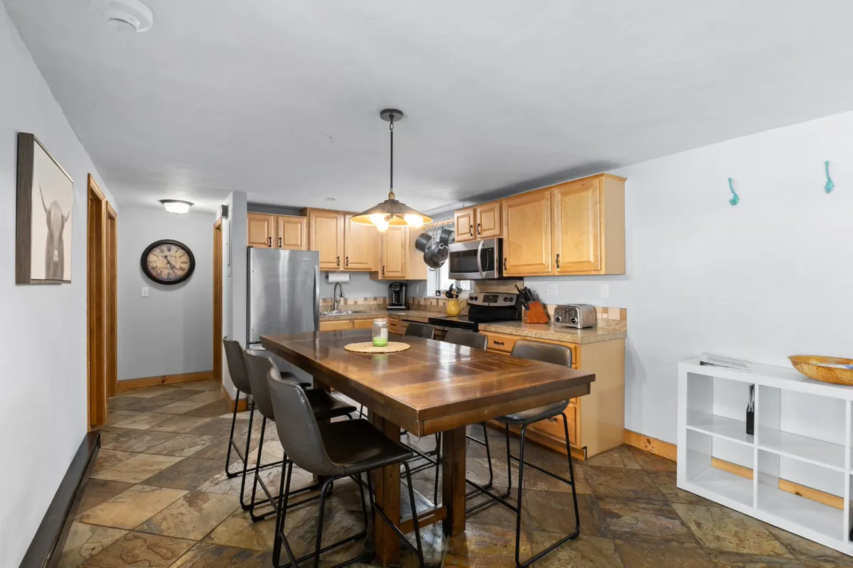 A spacious dining area with a large wooden table set for family meals or casual gatherings. Stainless steel appliances and a modern light fixture lend a contemporary feel, while decorative wall art adds personality, setting the scene for group meals and celebrations.
